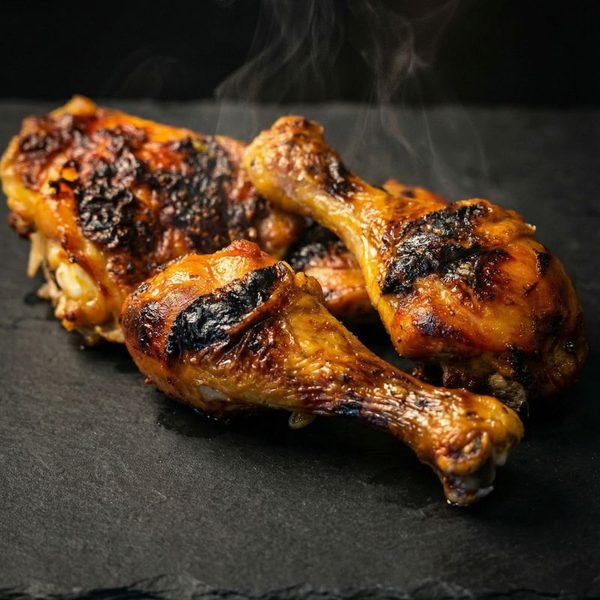 Three smoking chicken drumsticks resting on dark slate, deep caramelized crust with steam rising off the surface
